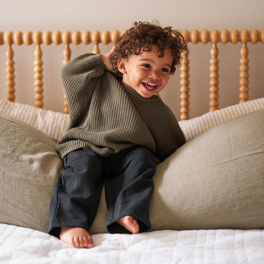 Child sitting on a bed with a wooden headboard, smiling.