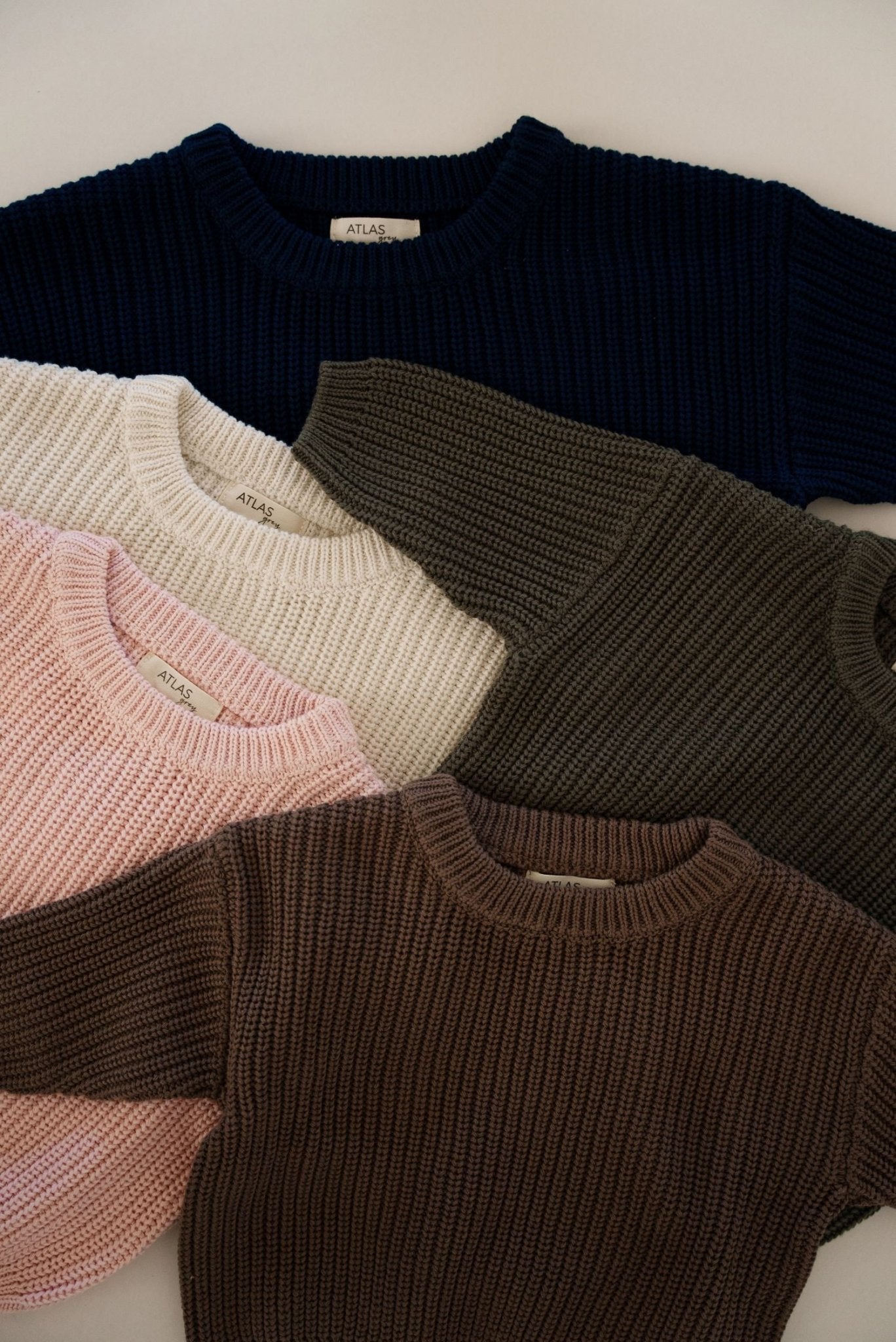 Five knit sweaters in different colors arranged on a light background