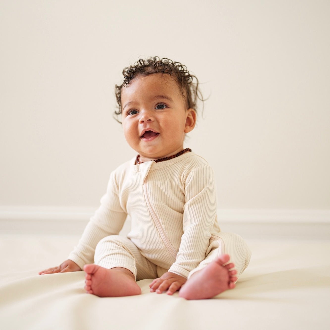 Baby in a white onesie sitting on a white surface