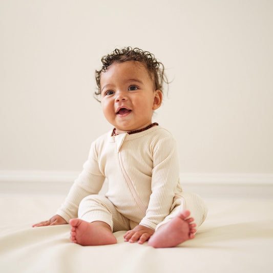 Baby in a white onesie sitting on a white surface