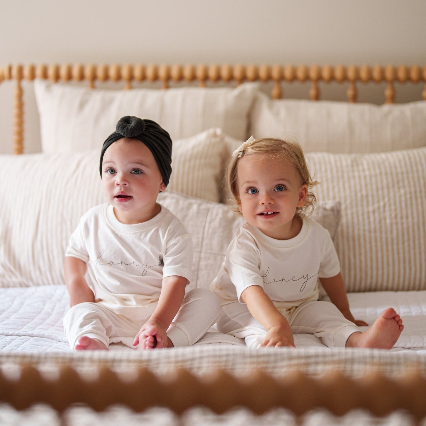 Two children sitting on a bed wearing matching outfits with the word 'honey' printed on them.