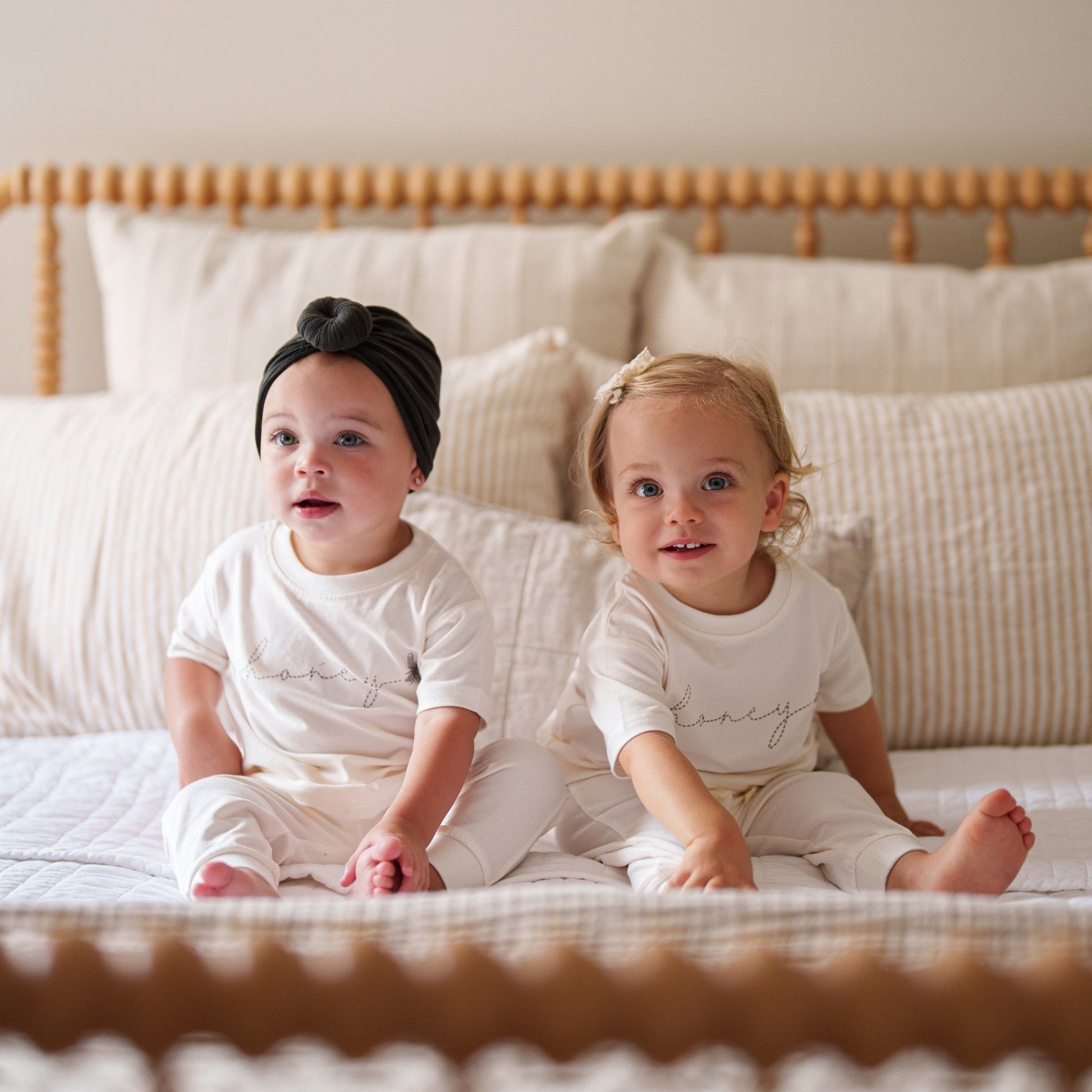Two children sitting on a bed wearing matching outfits with the word 'honey' printed on them.