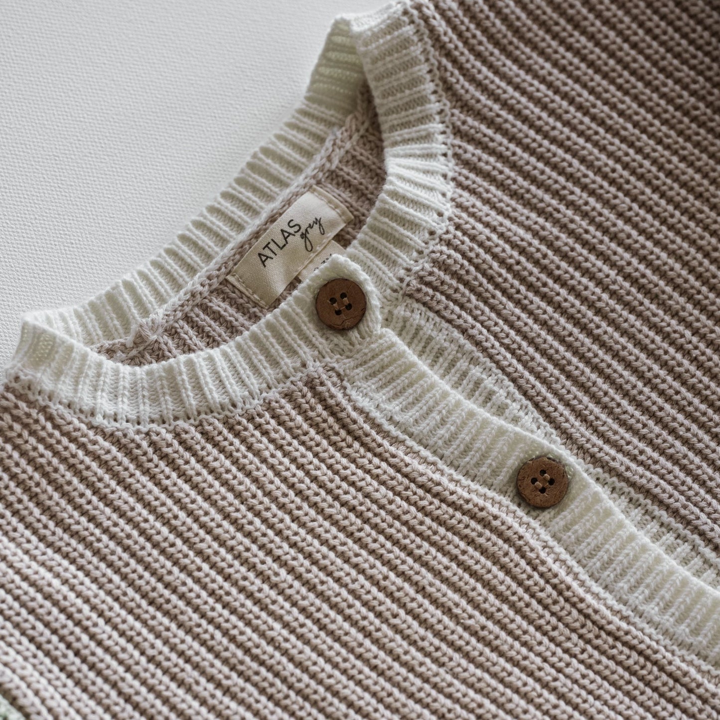 Close-up of a ribbed knit sweater with button details on a light background