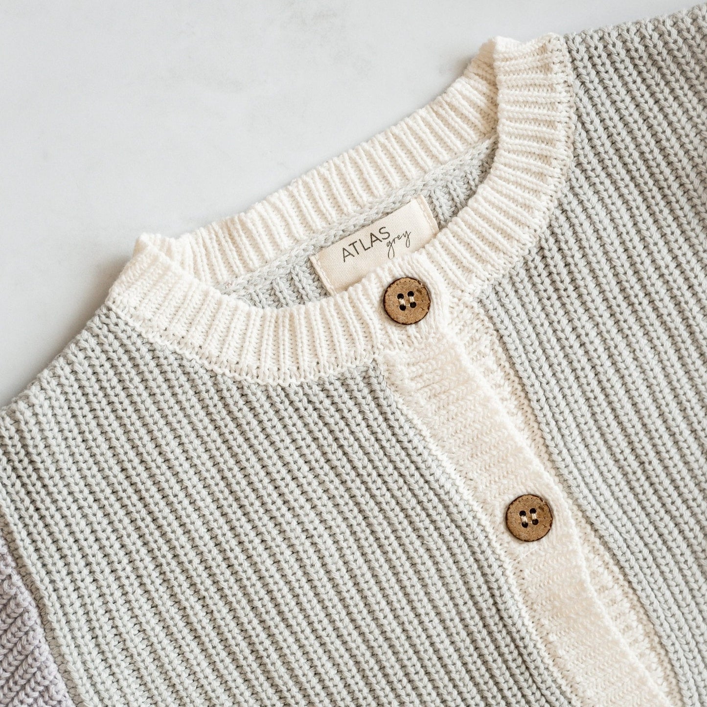 Close-up of a knitted cardigan with buttons and a visible brand label on a light gray background.