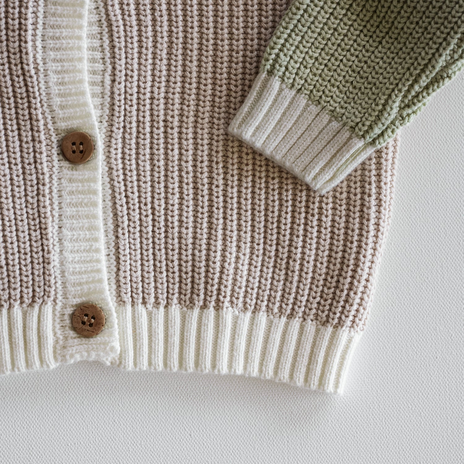 Close-up of a knitted cardigan with brown buttons on a white background
