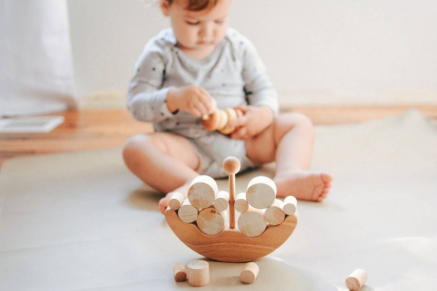 Baby sitting on a blanket on the floor playing with wooden balancing boat