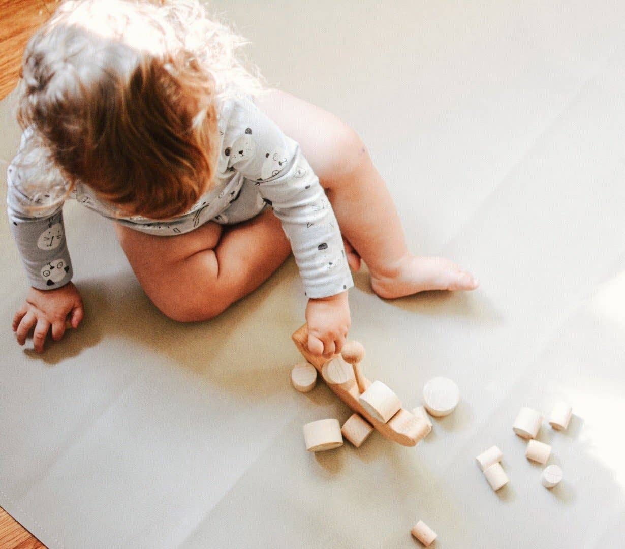 Baby sitting on a blanket on the floor playing with wooden balance boat