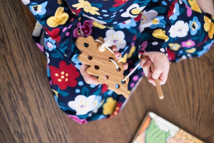 toddler sitting on the floor playing with lacing oak leaf toy