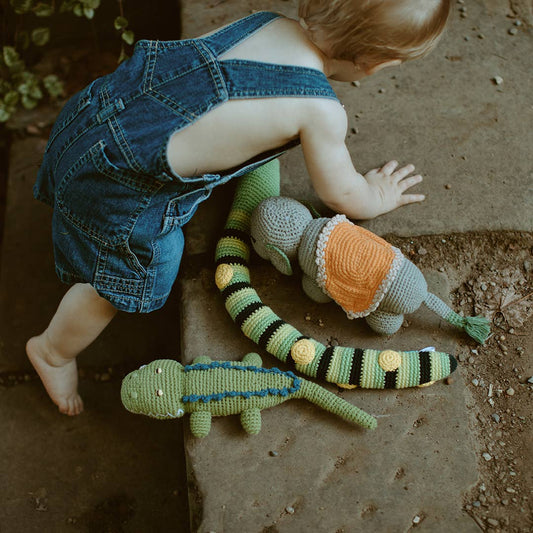Baby in denim overalls playing with crocheted toys on a stone surface