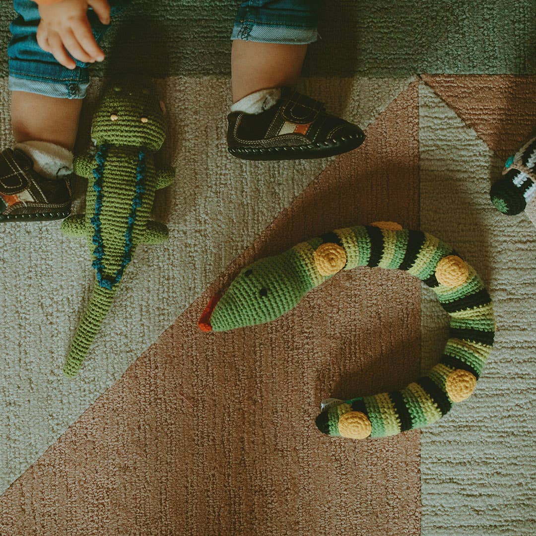 Knitted toy snake on a textured carpet with children's feet in the background