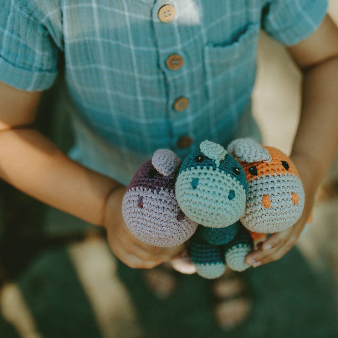 Child holding three crocheted dinosaur toys in their hands.