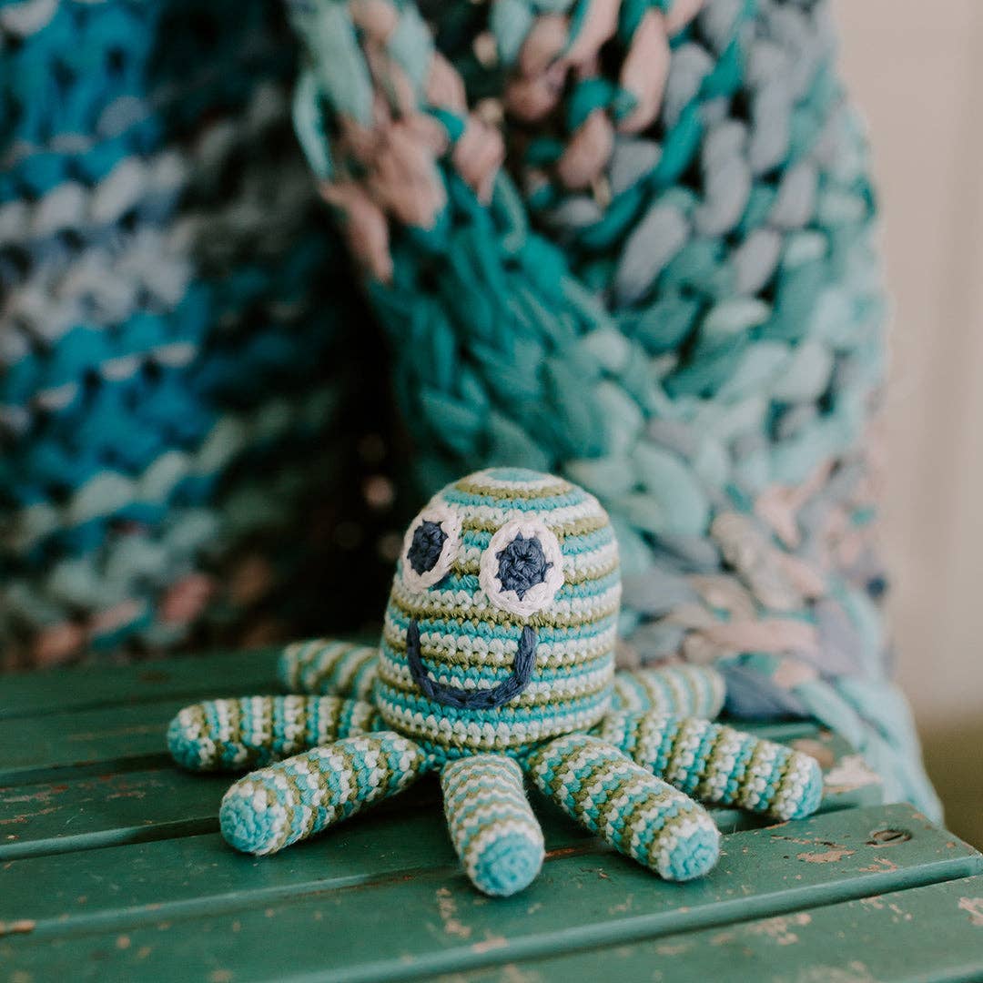 Crocheted octopus toy on a wooden surface with a textured teal blanket in the background