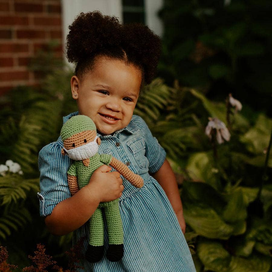 Child holding a hospital hero doll  in front of a brick wall and greenery