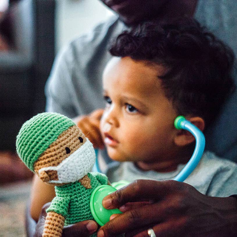 Child playing with a toy doctor doll and stethoscope, held by an adult.