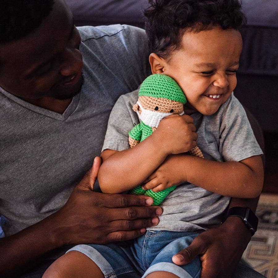 Child holding a doll while sitting on an adult's lap, both smiling.