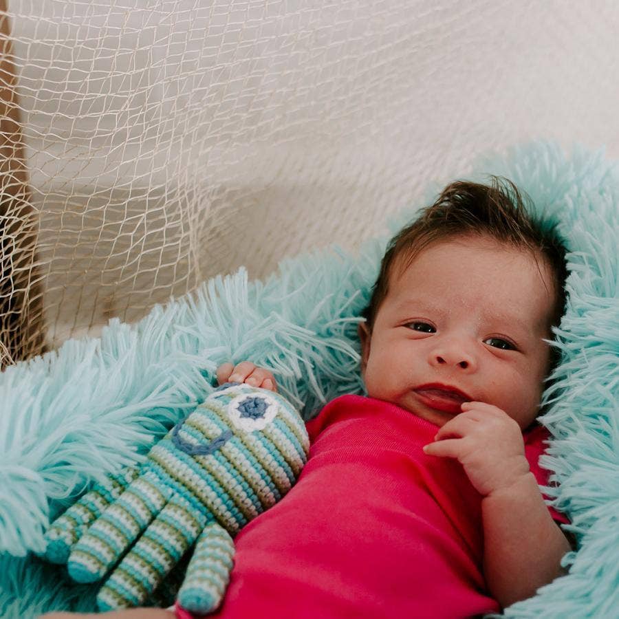 Baby lying on a textured surface with a knitted octopus next to it