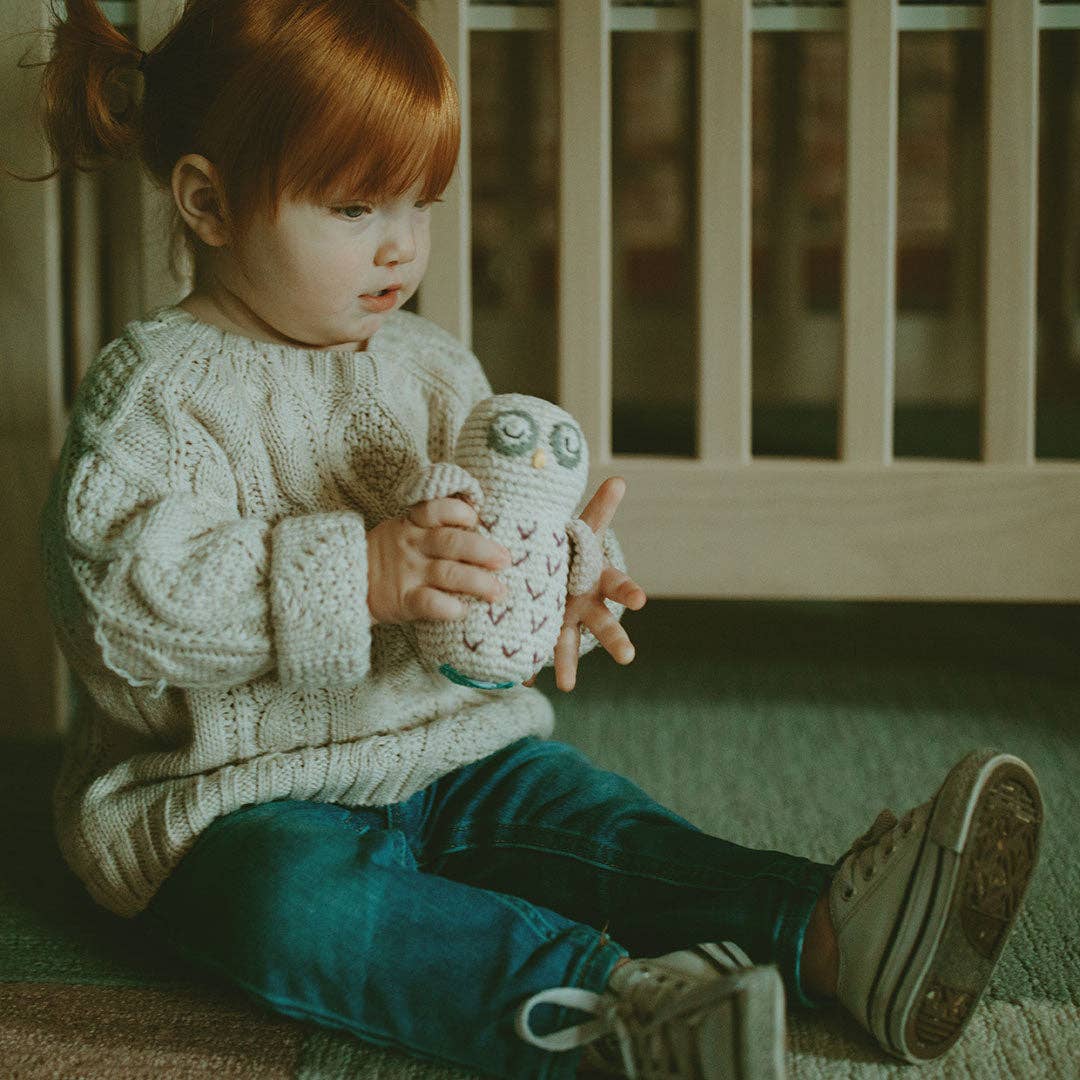 Child holding a knitted owl toy in a cozy indoor setting