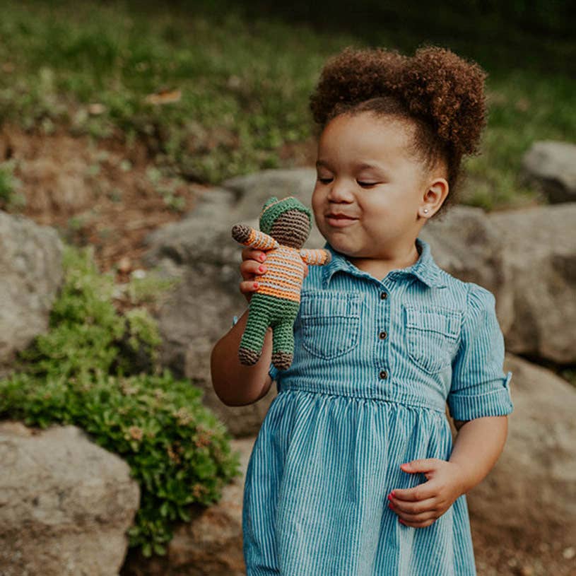 Child holding a knitted doll outdoors with rocks and grass in the background