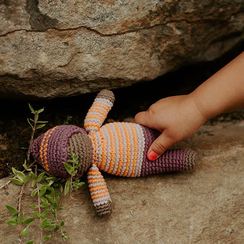 Hand holding a striped knitted doll against a stone background