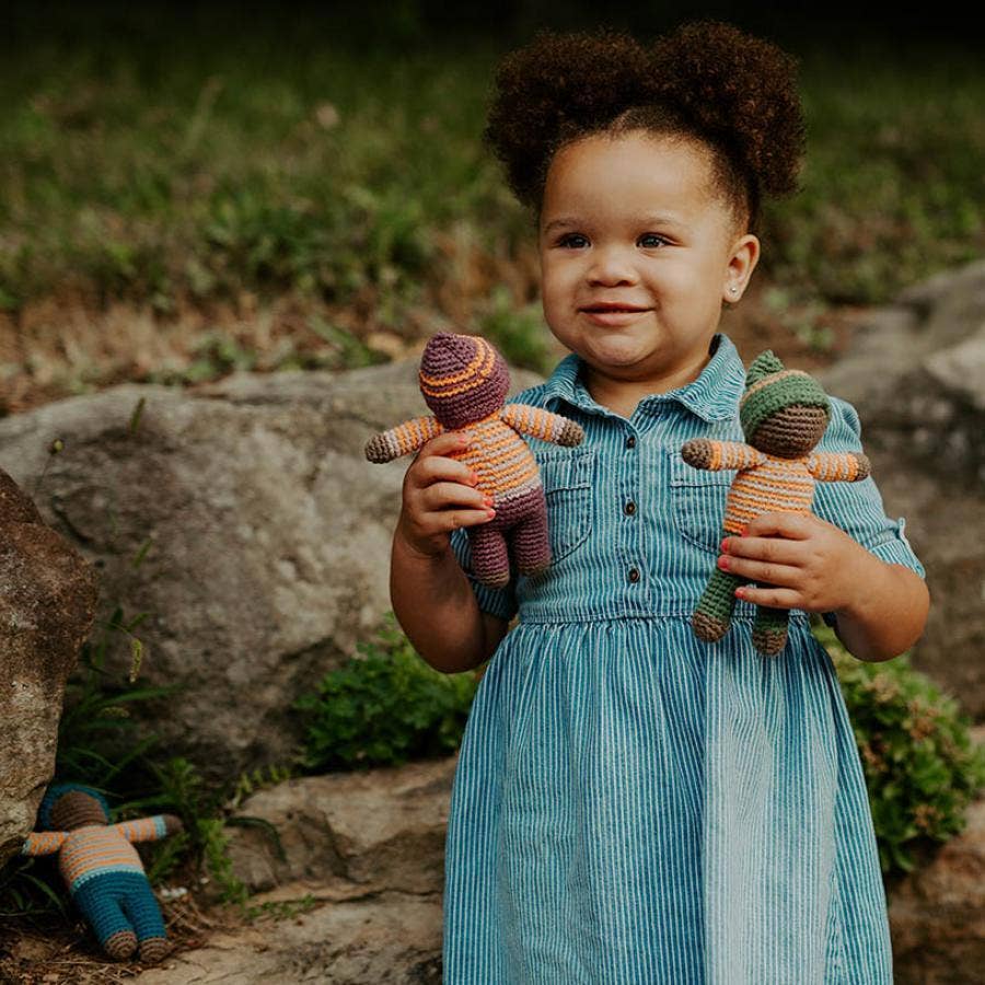 Child holding two knitted dolls outdoors with a natural background