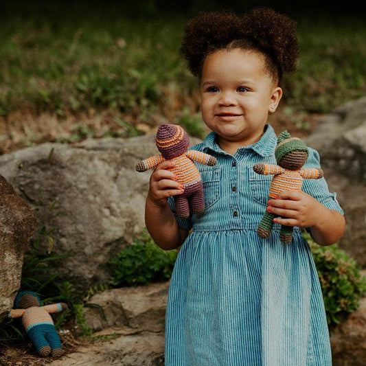 Child holding two knitted dolls outdoors with a natural background