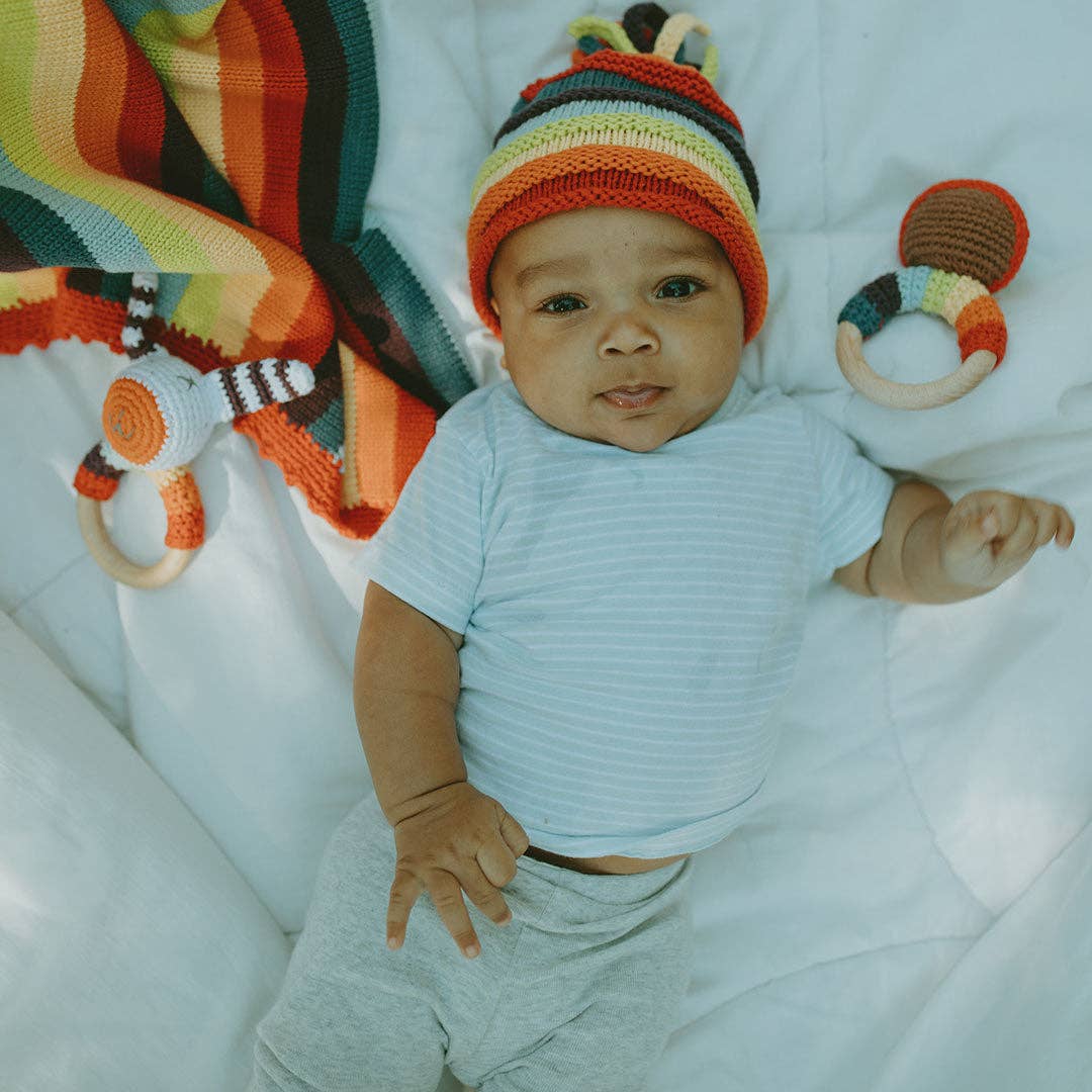 Baby wearing a rainbow knit hat with rainbow toys around on a white blanket