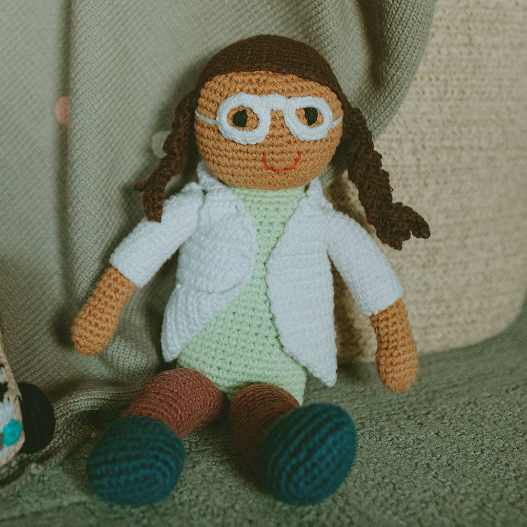 Crocheted doll with a lab coat and glasses on a textured surface