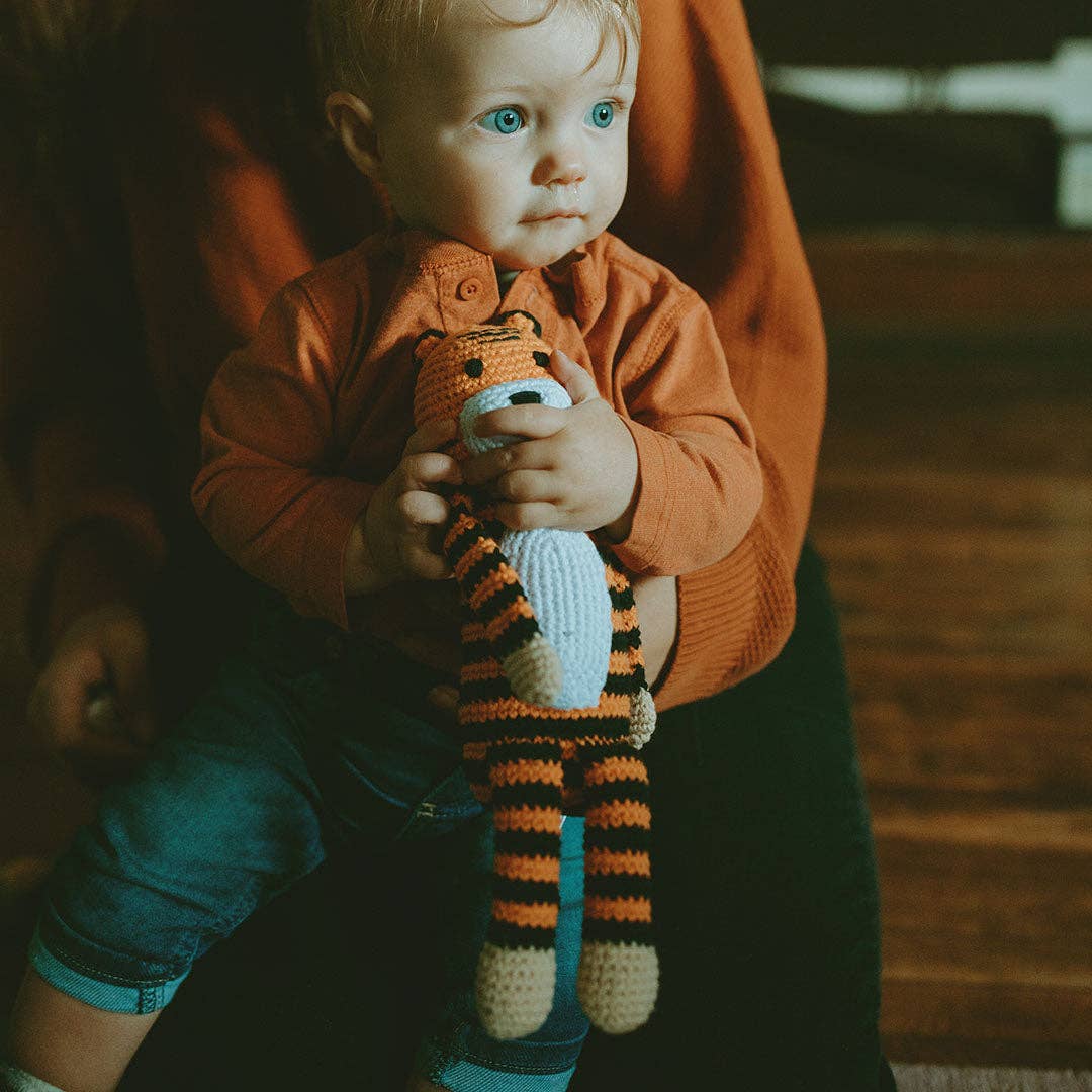 Baby holding a plus tiger toy while sitting in an adult's lap