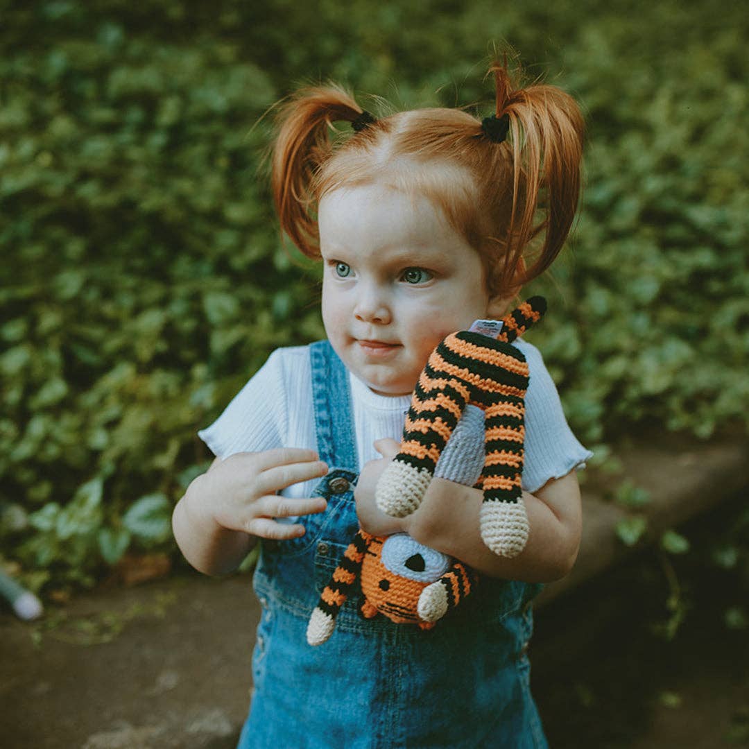 Child holding a tiger toy in front of a green leafy background