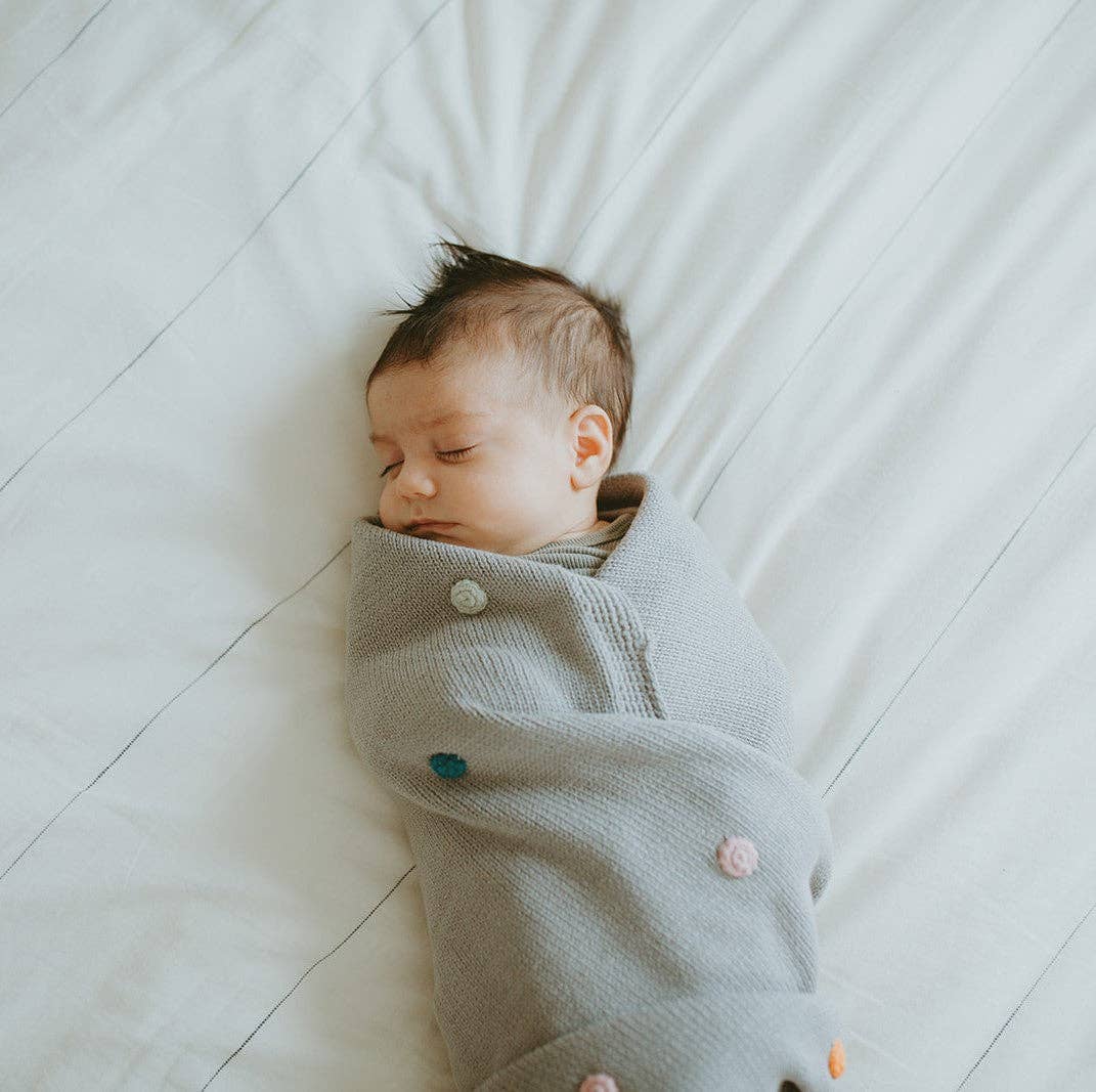 Newborn baby wrapped in a gray blanket on a white bed.