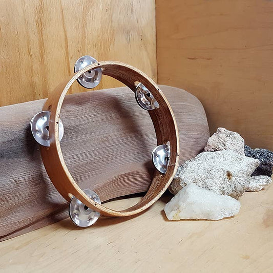 Wooden tambourine with metal jingles on a wooden surface with rocks.