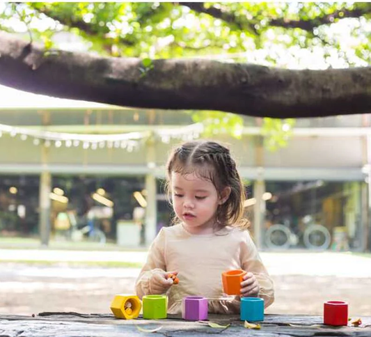 child playing out side at a table with the plan toys bee hive