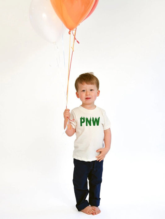 Child holding a balloon wearing organic cotton PNW trees kids tee