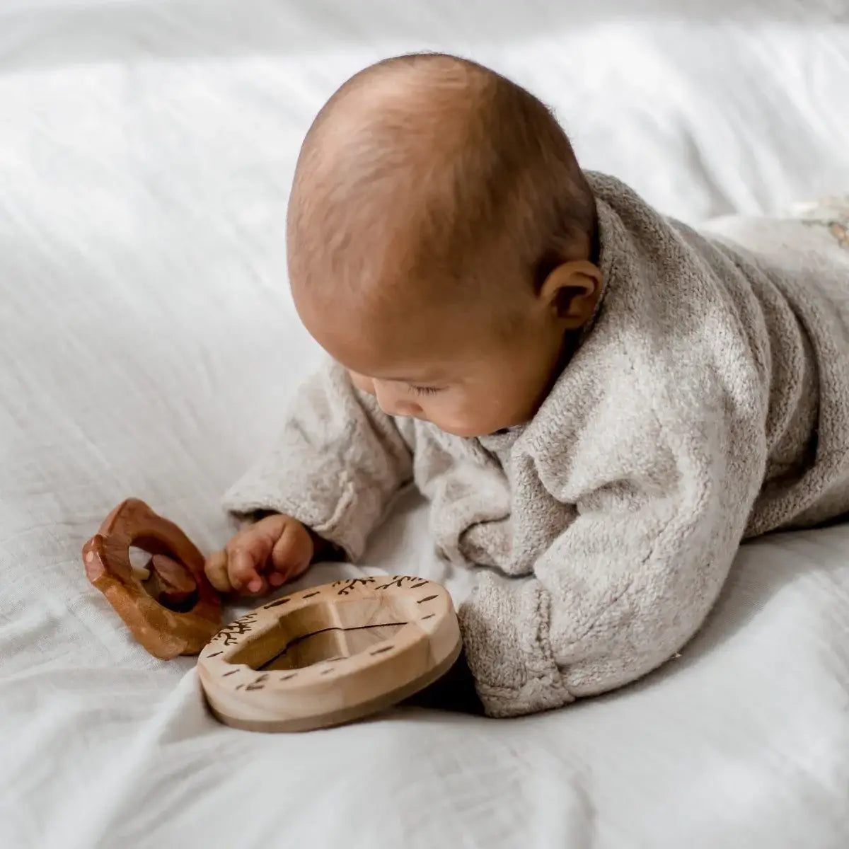 a baby laying on their stomach on a bed playing with a wooden baby gift set