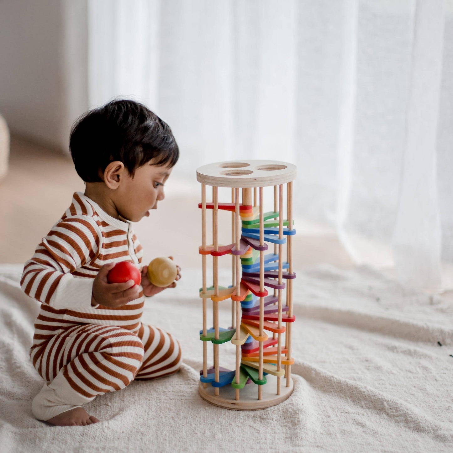 baby sitting on the floor wearing striped pajamas playing with pound-a-ball tower