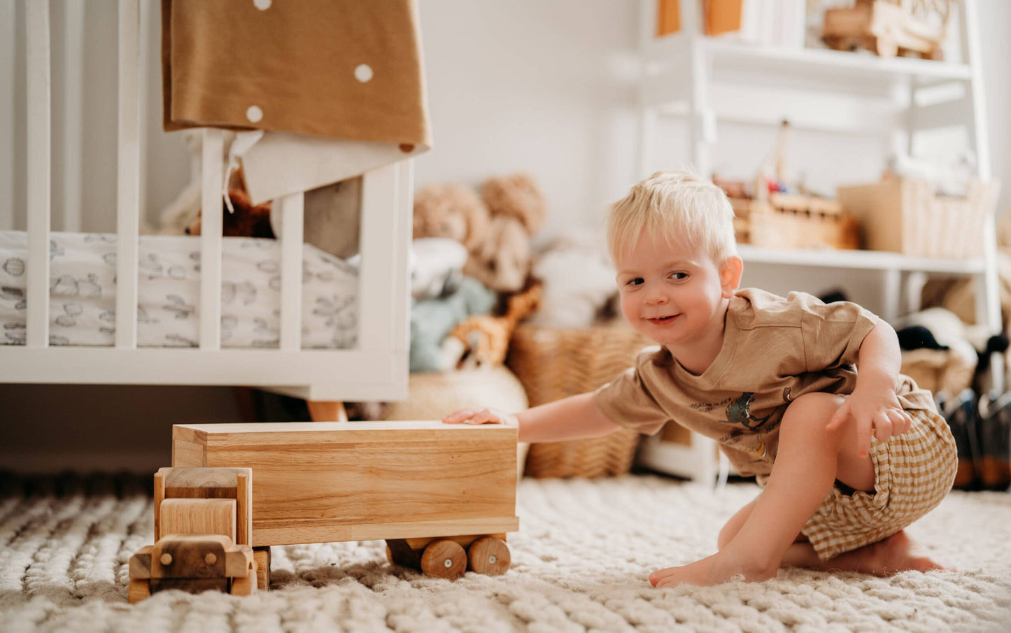 Child playing with a wooden truck in a room with shelves and toys.