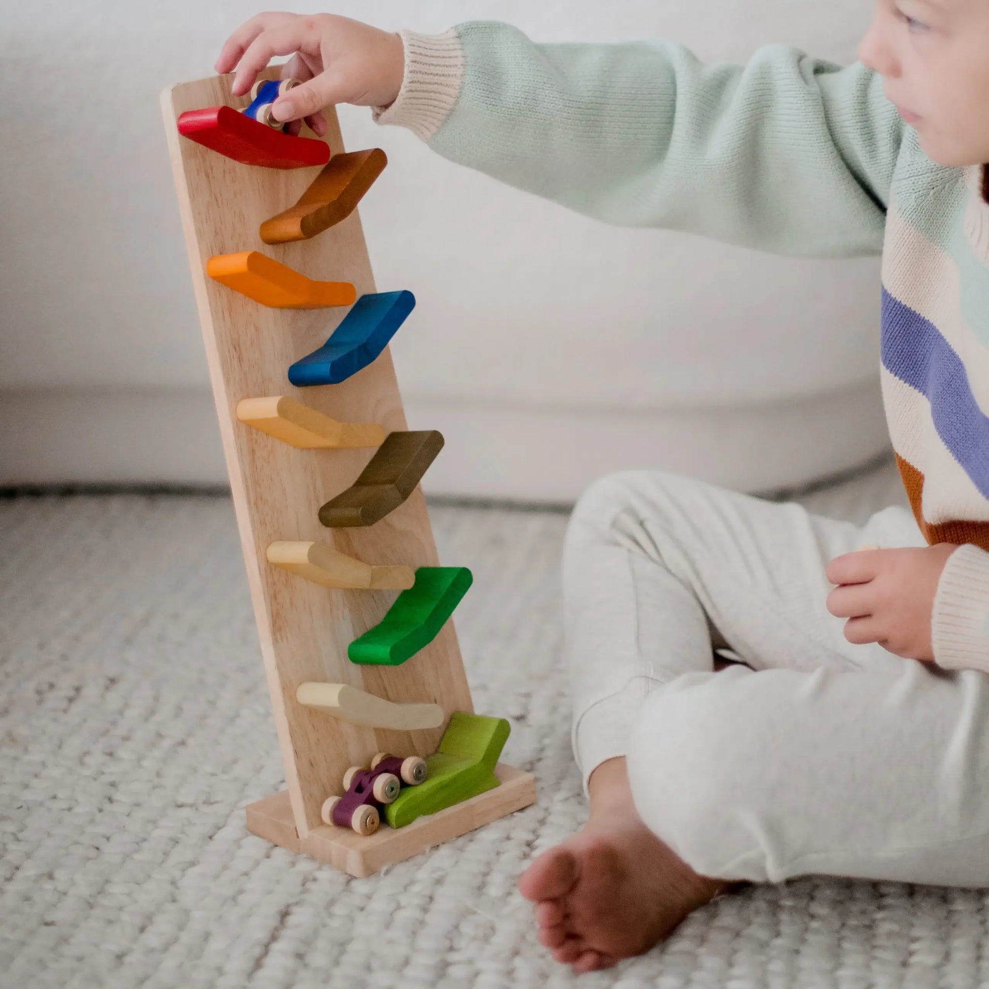 a child sitting on the floor playing with color zigzag racing cars