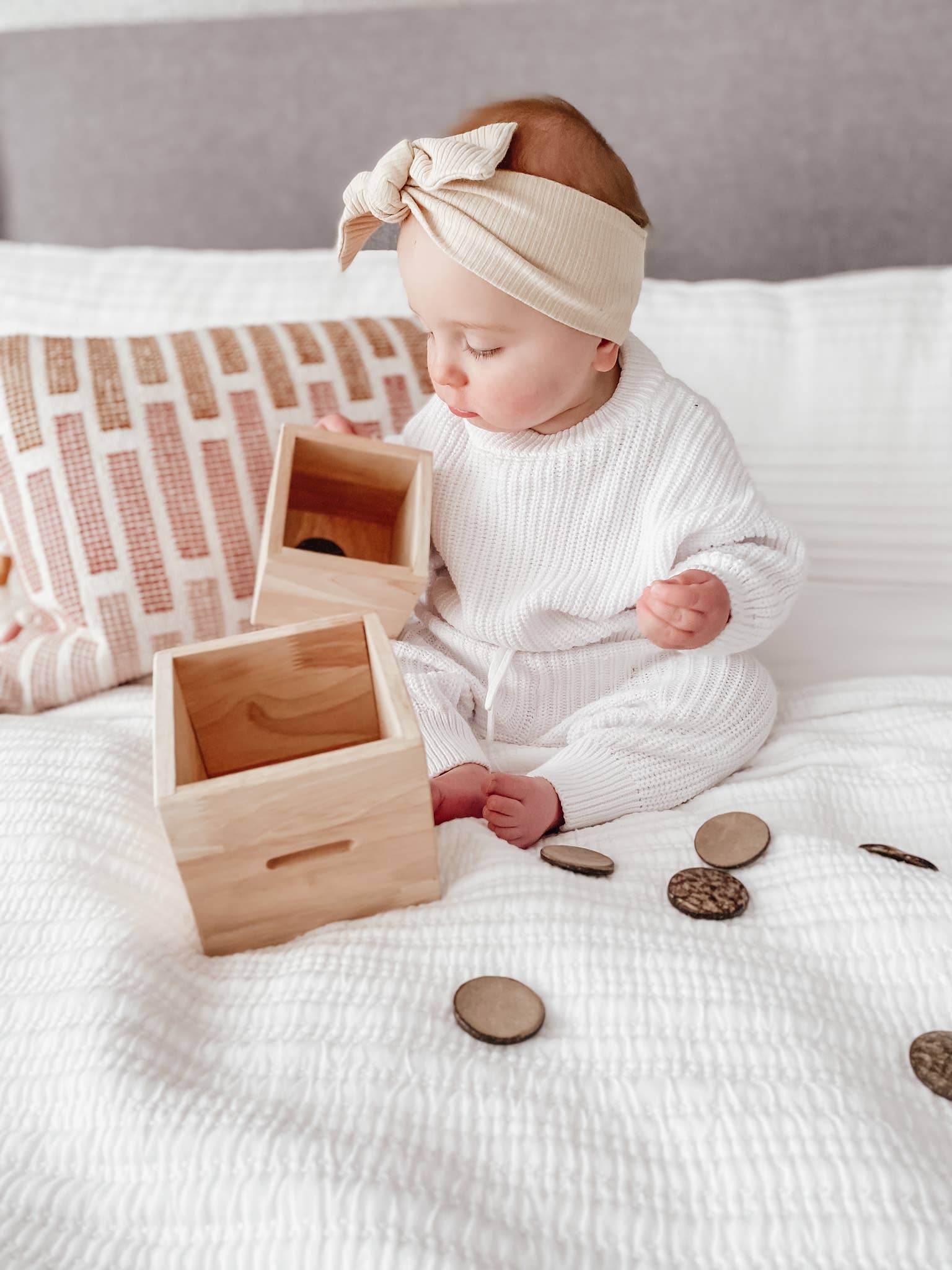 A baby playing with a wooden discs post box on a bed
