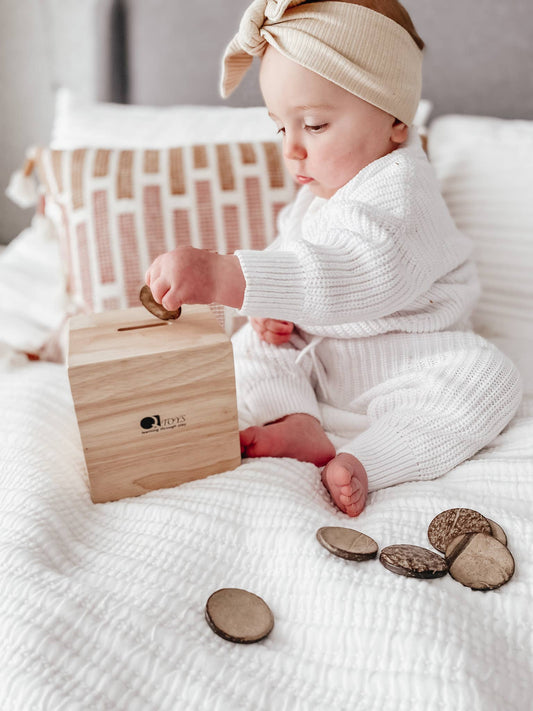 A baby playing with a wooden Montessori  disc box on a white blanket