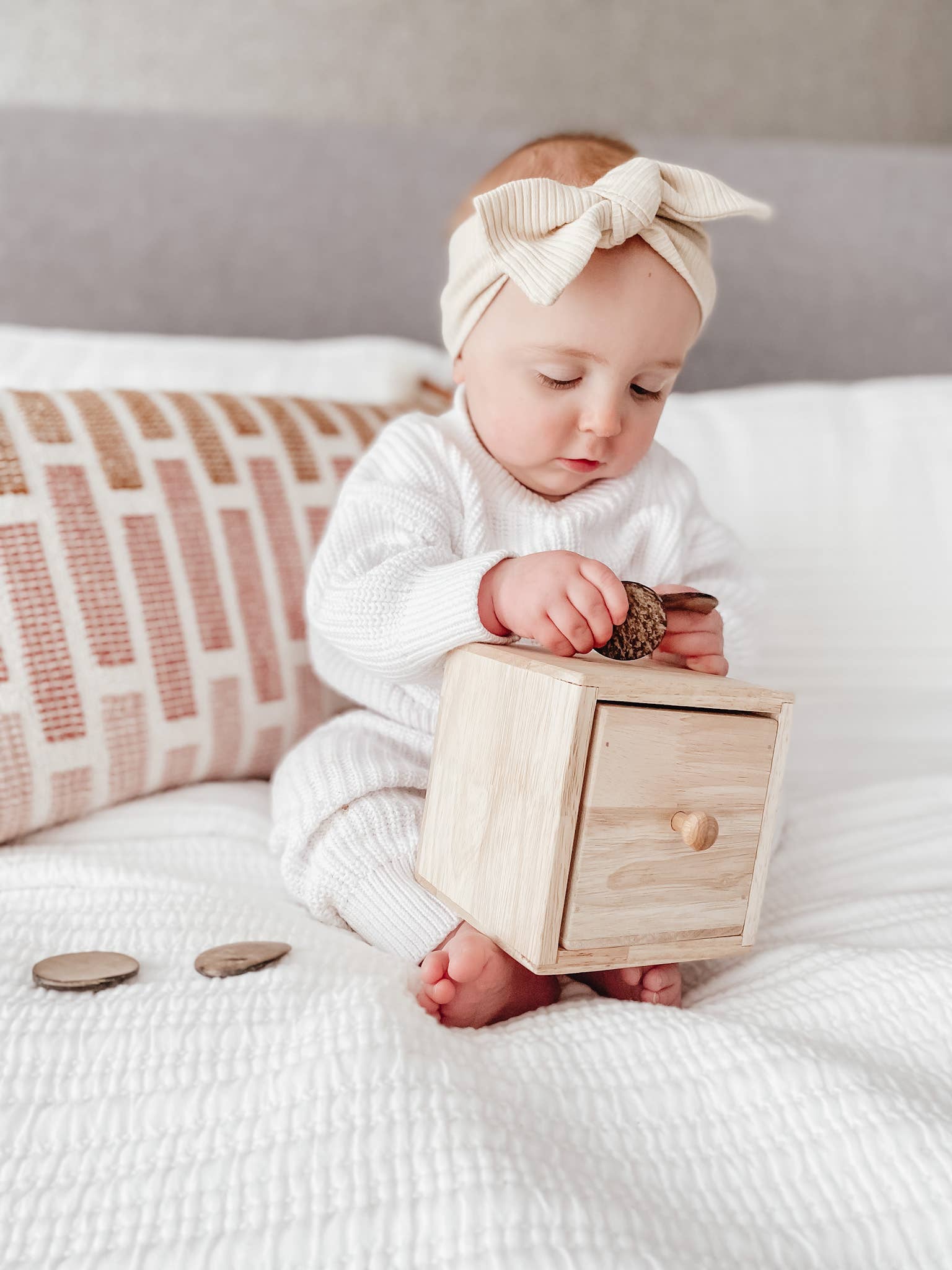 A baby playing with a wooden discs post box on a bed
