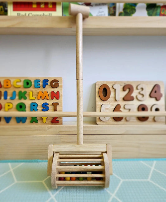 wooden mower push toy in front of a toy shelf