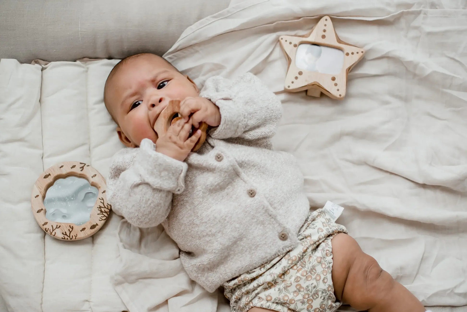 a baby laying on a bed wearing a wool cardigan playing with ocean baby gift set