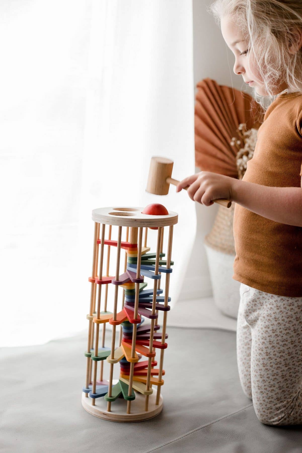 a child sitting on their knees on the floor playing with pound-a-ball tower