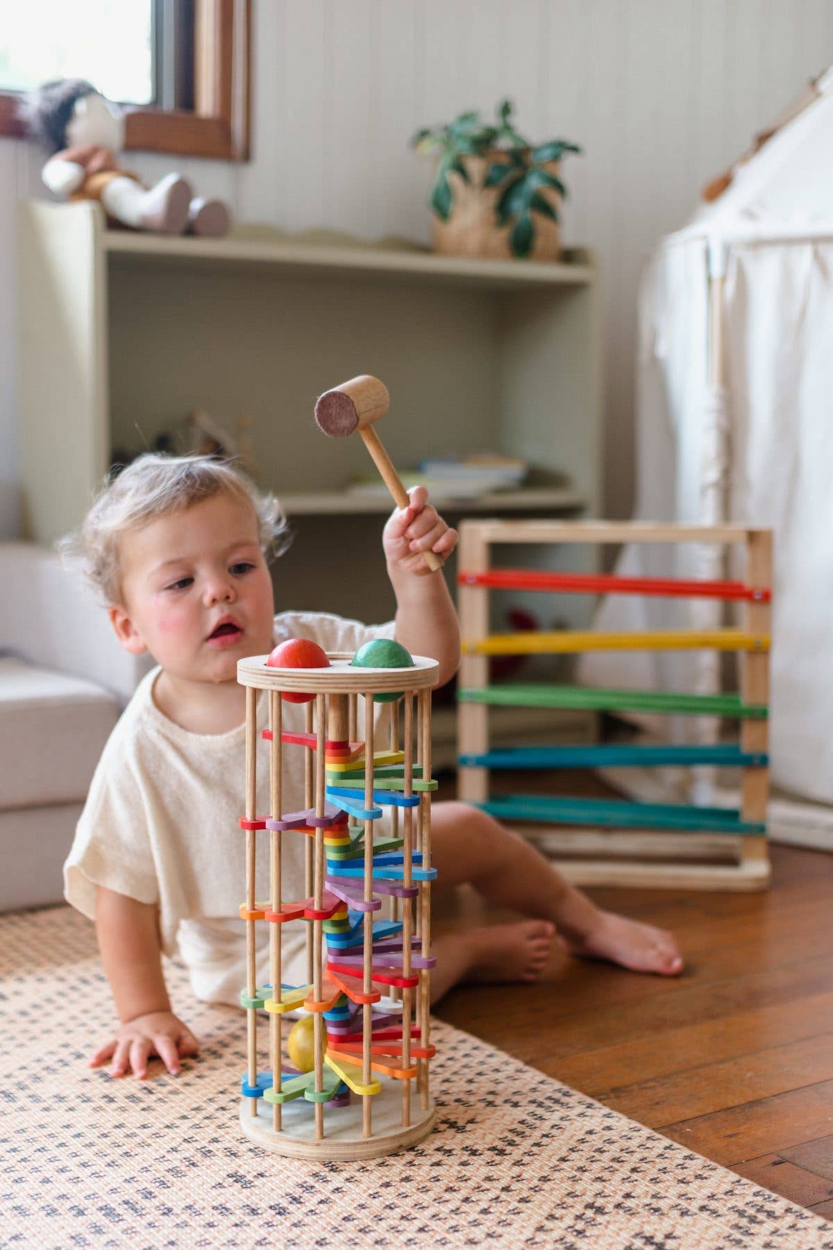 a toddler sitting on the floor holding a hammer to play with pound-a-ball tower