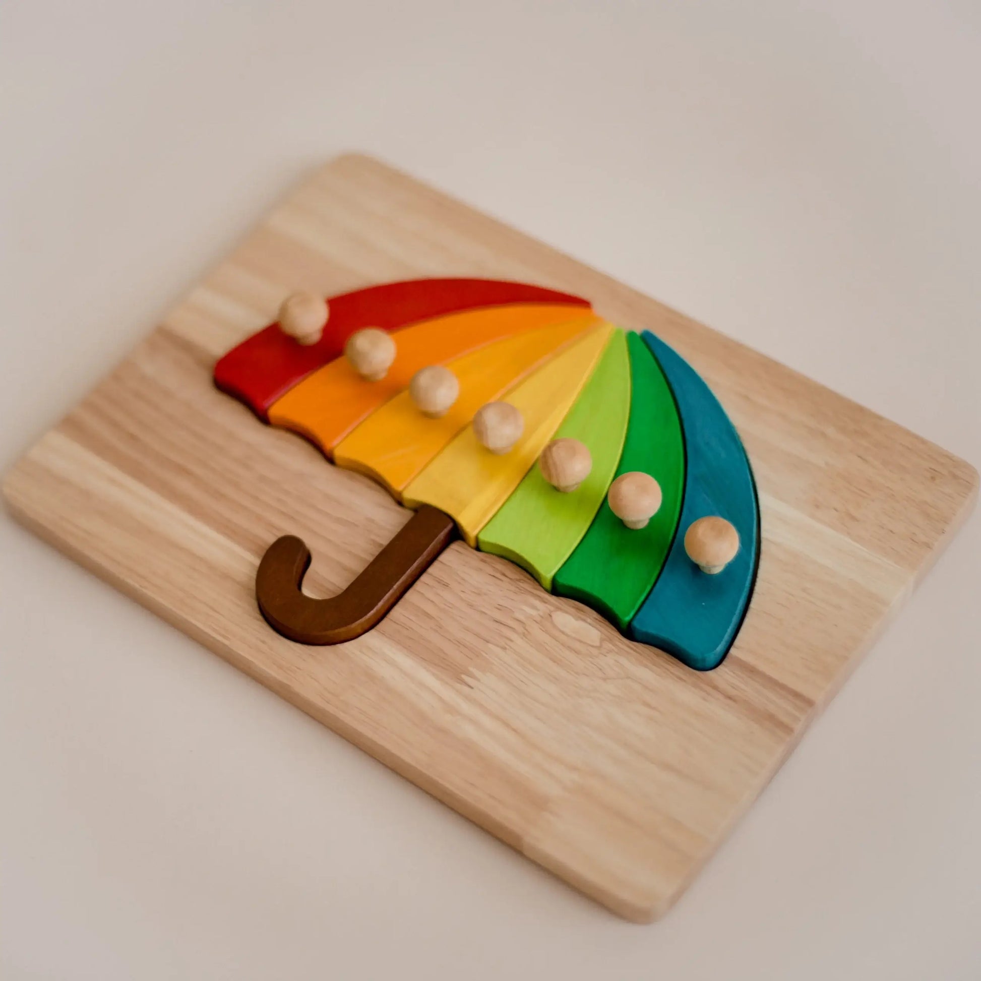 Wooden rainbow umbrella puzzle on a wooden base with a plain background