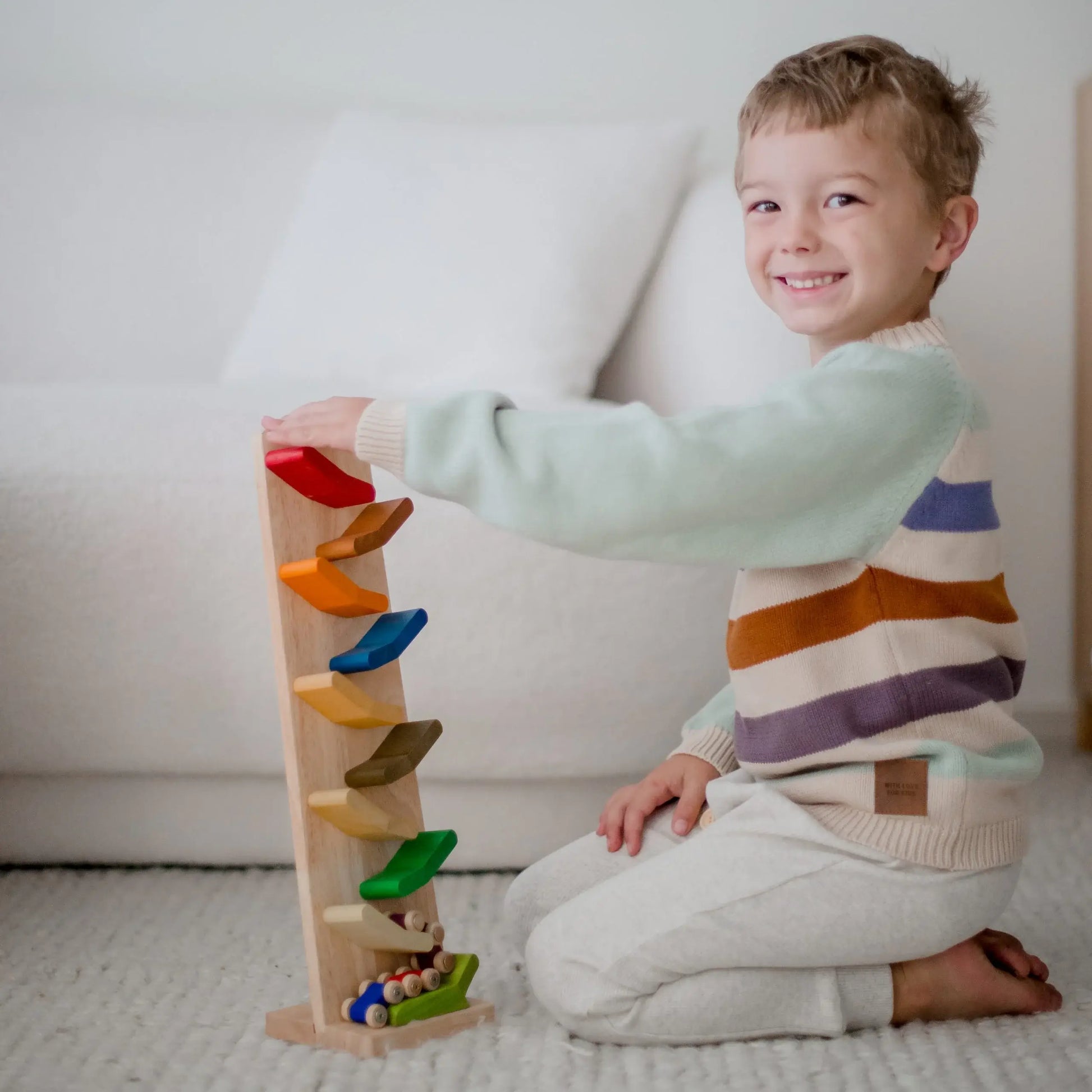 a child sitting on their knees on the floor playing with color zigzag racing cars