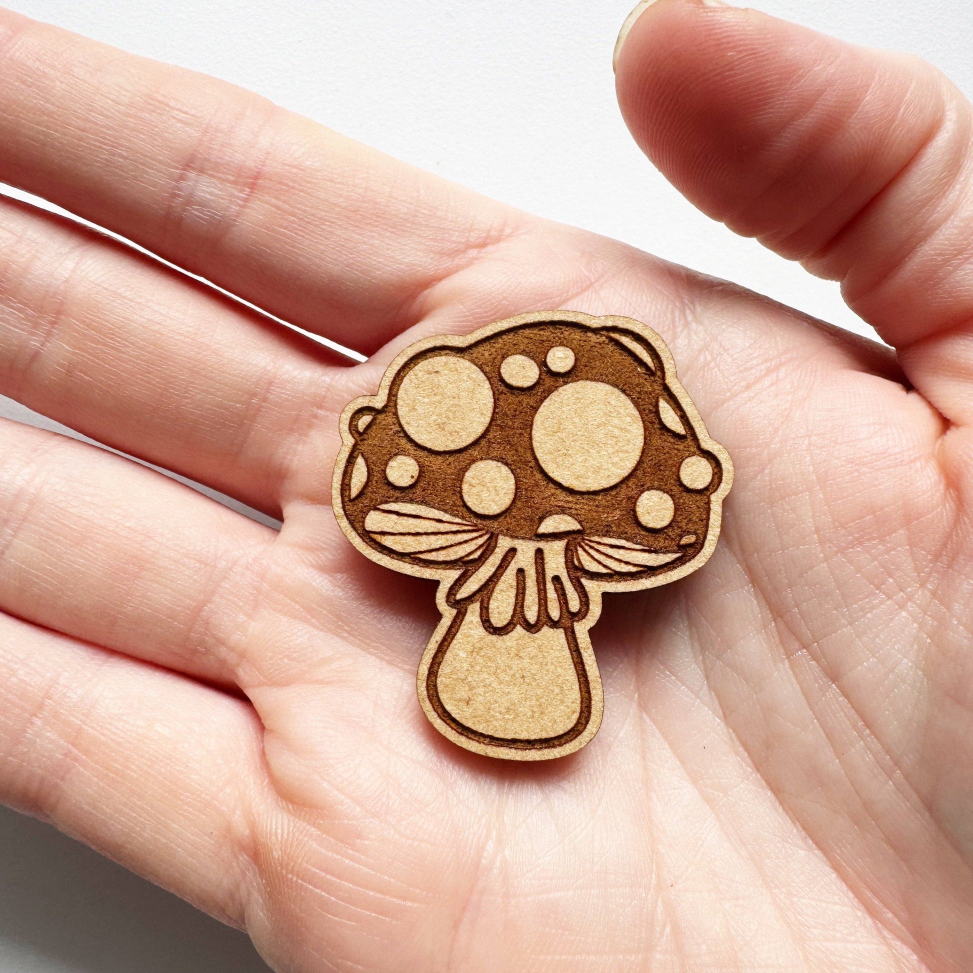 Wooden mushroom-shaped needleminder held in a hand against a white background