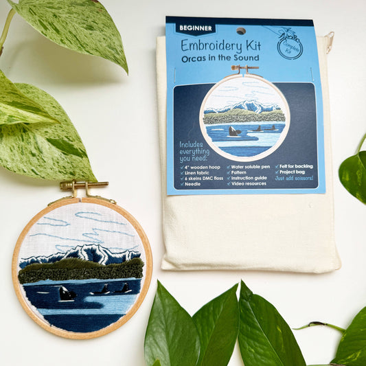 Embroidery kit with 'Orcas in the Sound' design and packaging on a white background with green leaves.