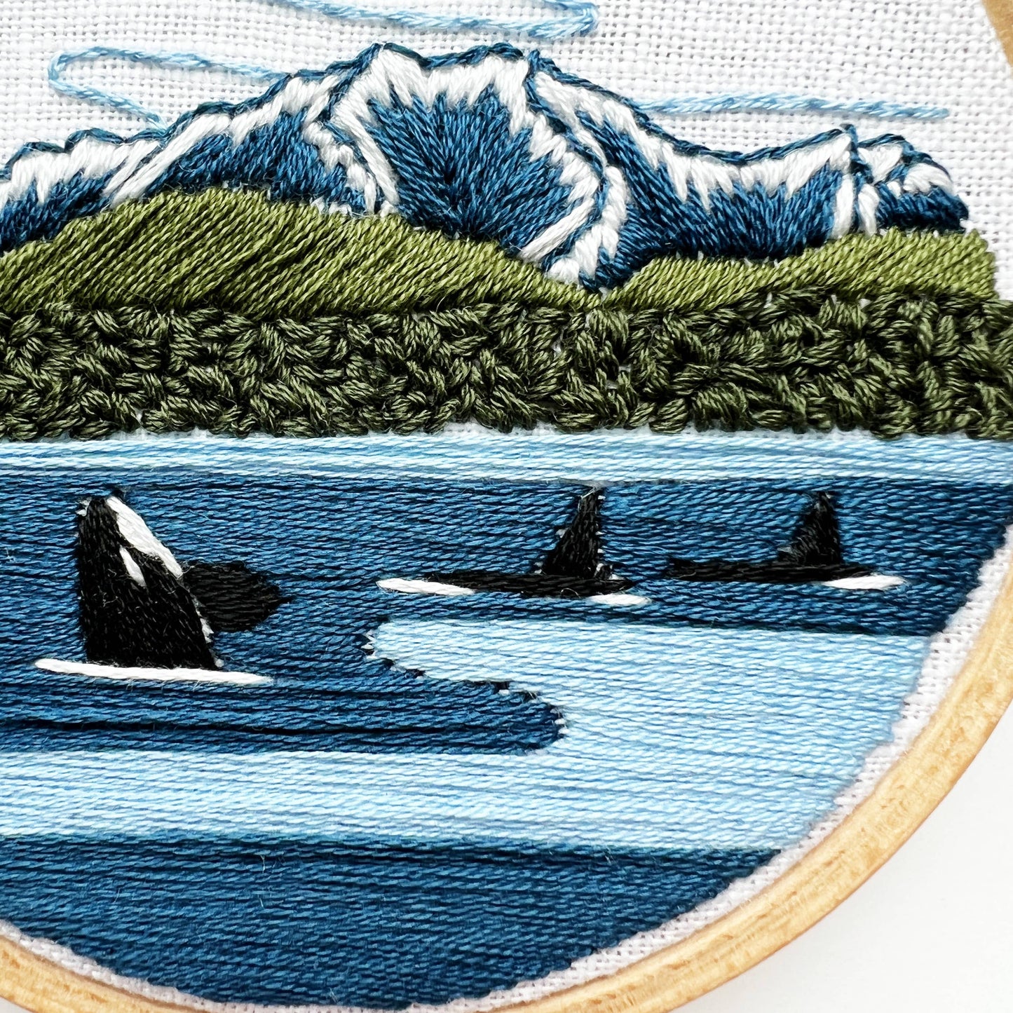 Embroidery of orcas in the ocean with a mountainous landscape.