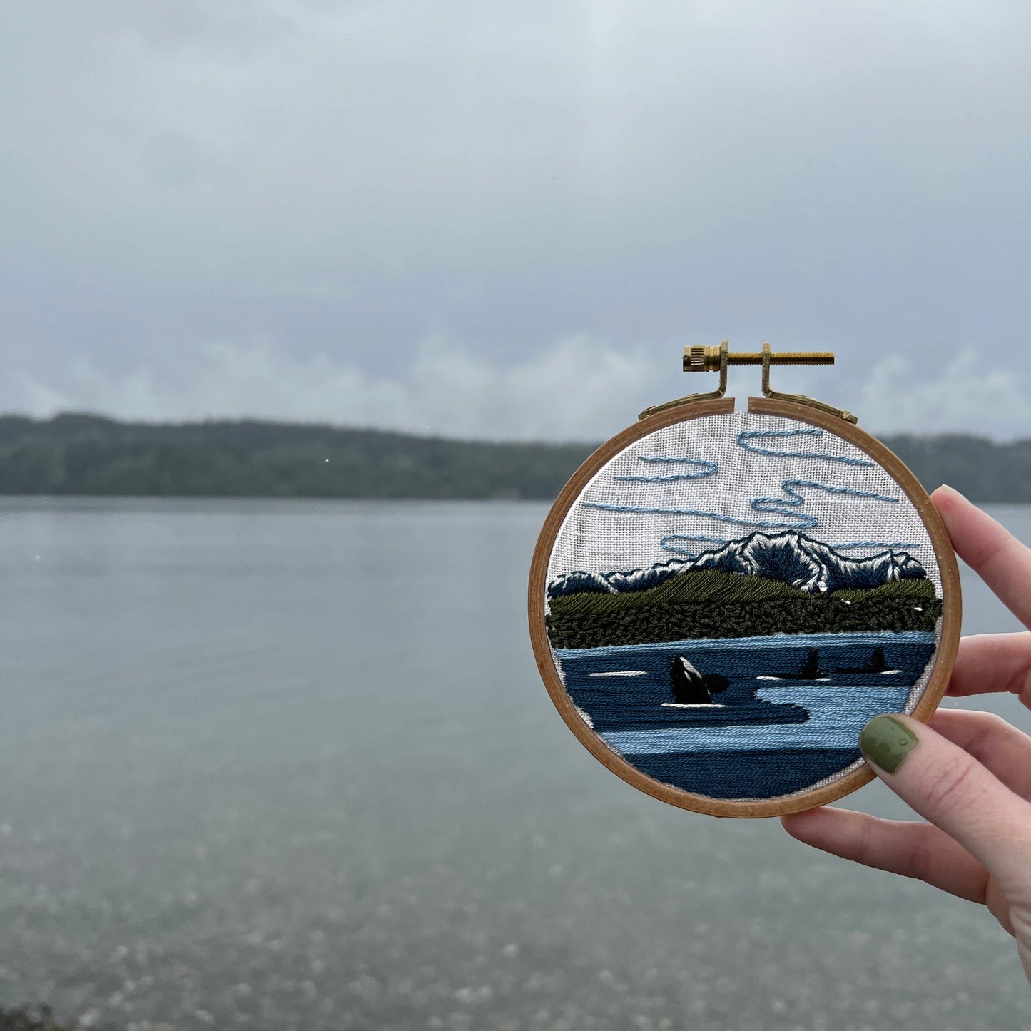 Embroidery hoop with a landscape design held over a lake